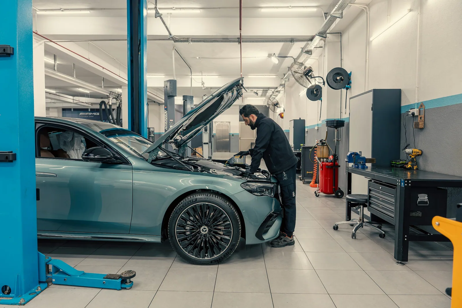 Ein Mechaniker prüft den Motorraum eines Autos mit geöffneter Motorhaube in einer hellen Werkstatt