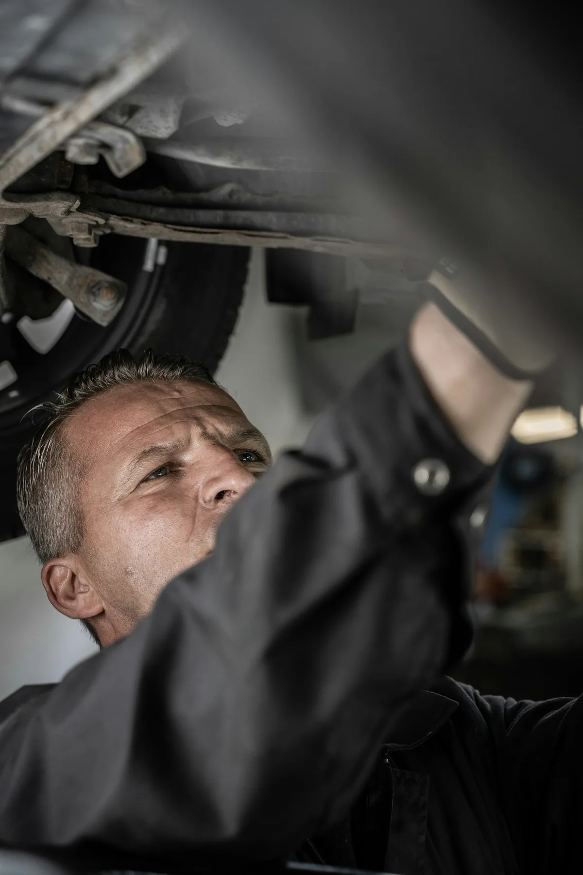 Ein Mechaniker prüft konzentriert den Unterboden eines Autos auf der Hebebühne